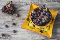 Δέσμη των κόκκινων σταφυλιών στο πορτοκαλί κύπελλο, στο ξύλινο κλίμα στοκ φωτογραφίες Δέσμη των κόκκινων σταφυλιών στο πορτοκαλί κύπελλο, στο ξύλινο κλίμα στοκ φωτογραφίες