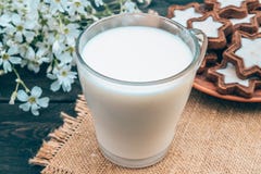 Δίπλα στο μπισκότο και τα άσπρα λουλούδια είναι ένα φλυτζάνι γυαλιού του γάλακτος σε μια πετσέτα στοκ φωτογραφία με δικαίωμα ελεύθερης χρήσης Δίπλα στο μπισκότο και τα άσπρα λουλούδια είναι ένα φλυτζάνι γυαλιού του γάλακτος σε μια πετσέτα στοκ φωτογραφία με δικαίωμα ελεύθερης χρήσης