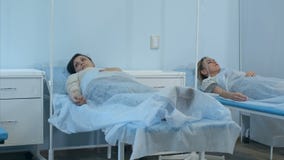 Δύο θηλυκοί ασθενείς στις σταλαγματιές που βρίσκονται στα κρεβάτια στο θάλαμο νοσοκομείων που ελέγχεται από δύο γιατρούς απόθεμα βίντεο Δύο θηλυκοί ασθενείς στις σταλαγματιές που βρίσκονται στα κρεβάτια στο θάλαμο νοσοκομείων που ελέγχεται από δύο γιατρούς απόθεμα βίντεο