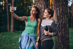 Δύο νέες αθλητικές φίλες που φορούν sportswear που κλίνει ενάντια στο δέντρο που παίρνει selfie με το smartphone στο δάσος στοκ φωτογραφίες με δικαίωμα ελεύθερης χρήσης Δύο νέες αθλητικές φίλες που φορούν sportswear που κλίνει ενάντια στο δέντρο που παίρνει selfie με το smartphone στο δάσος στοκ φωτογραφίες με δικαίωμα ελεύθερης χρήσης