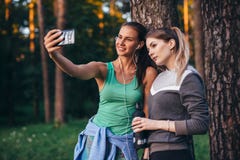Δύο νέες αθλητικές φίλες που φορούν sportswear που κλίνει ενάντια στο δέντρο που παίρνει selfie με το smartphone στο δάσος στοκ φωτογραφία με δικαίωμα ελεύθερης χρήσης Δύο νέες αθλητικές φίλες που φορούν sportswear που κλίνει ενάντια στο δέντρο που παίρνει selfie με το smartphone στο δάσος στοκ φωτογραφία με δικαίωμα ελεύθερης χρήσης