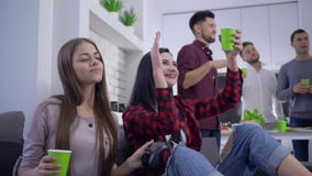 Ελεύθερος χρόνος, συνεδρίαση χορού φίλων στον καναπέ με την κονσόλα και φλυτζάνια εγγράφου στα χέρια στο backgrounf των ανθρώπων φιλμ μικρού μήκους Ελεύθερος χρόνος, συνεδρίαση χορού φίλων στον καναπέ με την κονσόλα και φλυτζάνια εγγράφου στα χέρια στο backgrounf των ανθρώπων φιλμ μικρού μήκους
