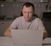 Ελκυστική συνεδρίαση ατόμων το βράδυ στην κουζίνα με ένα lap-top στοκ εικόνα με δικαίωμα ελεύθερης χρήσης Ελκυστική συνεδρίαση ατόμων το βράδυ στην κουζίνα με ένα lap-top στοκ εικόνα με δικαίωμα ελεύθερης χρήσης