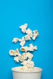 Επιπλέον popcorn από ένα φλυτζάνι της Λευκής Βίβλου σε ένα μπλε υπόβαθρο στοκ εικόνα Επιπλέον popcorn από ένα φλυτζάνι της Λευκής Βίβλου σε ένα μπλε υπόβαθρο στοκ εικόνα