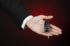 Επιχείρηση και θέμα δώρων: ο πωλητής αυτοκινήτων σε ένα μαύρο κοστούμι κρατά τα κλειδιά σε ένα νέο αυτοκίνητο σε ένα σκούρο κόκκι Στοκ εικόνα με δικαίωμα ελεύθερης χρήσης Επιχείρηση και θέμα δώρων: ο πωλητής αυτοκινήτων σε ένα μαύρο κοστούμι κρατά τα κλειδιά σε ένα νέο αυτοκίνητο σε ένα σκούρο κόκκι Στοκ εικόνα με δικαίωμα ελεύθερης χρήσης