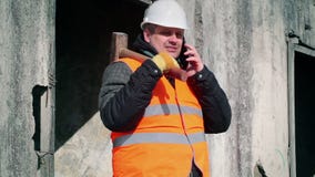 Εργαζόμενος με το τηλέφωνο κυττάρων και σφυρί ελκήθρων κοντά στον τοίχο φιλμ μικρού μήκους Εργαζόμενος με το τηλέφωνο κυττάρων και σφυρί ελκήθρων κοντά στον τοίχο φιλμ μικρού μήκους