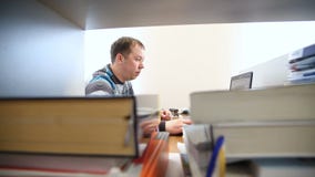 Εργασίες μηχανικών στον υπολογιστή στο υπόβαθρο των βιβλίων και των περιοδικών απόθεμα βίντεο Εργασίες μηχανικών στον υπολογιστή στο υπόβαθρο των βιβλίων και των περιοδικών απόθεμα βίντεο