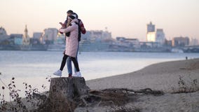 Ευτυχές νέο ζεύγος που περπατά στην παραλία το φθινόπωρο στα πλαίσια του ποταμού που γίνεται στο κολόβωμα που χαμογελά και φιλμ μικρού μήκους Ευτυχές νέο ζεύγος που περπατά στην παραλία το φθινόπωρο στα πλαίσια του ποταμού που γίνεται στο κολόβωμα που χαμογελά και φιλμ μικρού μήκους