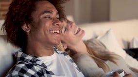 Ευτυχές νέο ζεύγος που προσέχει τη TV μαζί καθμένος στον καναπέ στο σπίτι Ευτυχές νέο ζεύγος που προσέχει τη TV μαζί καθμένος στον καναπέ στο σπίτι