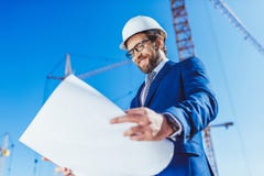 Ευτυχής επιχειρηματίας hardhat και κοστούμι που εξετάζει την οικοδόμηση των σχεδίων στοκ φωτογραφία Ευτυχής επιχειρηματίας hardhat και κοστούμι που εξετάζει την οικοδόμηση των σχεδίων στοκ φωτογραφία