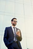 Ευτυχής νεαρός άνδρας σε ένα μοντέρνο κοστούμι και τα γυαλιά ηλίου που στέκονται μπροστά από τα γραφεία με το τηλέφωνο Στοκ φωτογραφία με δικαίωμα ελεύθερης χρήσης Ευτυχής νεαρός άνδρας σε ένα μοντέρνο κοστούμι και τα γυαλιά ηλίου που στέκονται μπροστά από τα γραφεία με το τηλέφωνο Στοκ φωτογραφία με δικαίωμα ελεύθερης χρήσης