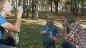 Ευτυχείς φυσώντας φυσαλίδες μητέρων, πατέρων και γιων στο πάρκο στοκ εικόνες Ευτυχείς φυσώντας φυσαλίδες μητέρων, πατέρων και γιων στο πάρκο στοκ εικόνες
