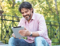 Εύθυμο ενήλικο άτομο που κρατά την ψηφιακή ταμπλέτα του και που κάνει σερφ στο πάρκο Στοκ Εικόνες Εύθυμο ενήλικο άτομο που κρατά την ψηφιακή ταμπλέτα του και που κάνει σερφ στο πάρκο Στοκ Εικόνες