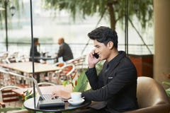 Εύθυμος επιχειρηματίας που εργάζεται στον πίνακα καφέδων στοκ εικόνα Εύθυμος επιχειρηματίας που εργάζεται στον πίνακα καφέδων στοκ εικόνα