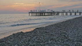 Ζωηρόχρωμο ηλιοβασίλεμα στη θάλασσα Όμορφη χαλικιώδης παραλία με τα κύματα και την αποβάθρα απόθεμα βίντεο Ζωηρόχρωμο ηλιοβασίλεμα στη θάλασσα Όμορφη χαλικιώδης παραλία με τα κύματα και την αποβάθρα απόθεμα βίντεο
