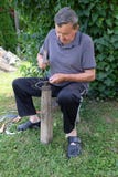 Η Farmer με το εργαλείο σφυριών και σιδήρου στο κολόβωμα δέντρων ακονίζει το δρεπάνι του στοκ φωτογραφίες Η Farmer με το εργαλείο σφυριών και σιδήρου στο κολόβωμα δέντρων ακονίζει το δρεπάνι του στοκ φωτογραφίες