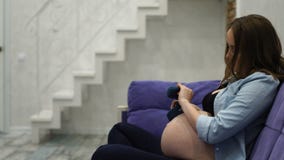 Η έγκυος γυναίκα που κάθεται στο σπίτι σε μια πολυθρόνα που παίζει τις χαριτωμένες κάλτσες μωρών στο μωρό της, αυτό έχει προτείνε απόθεμα βίντεο Η έγκυος γυναίκα που κάθεται στο σπίτι σε μια πολυθρόνα που παίζει τις χαριτωμένες κάλτσες μωρών στο μωρό της, αυτό έχει προτείνε απόθεμα βίντεο