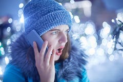 Η έκπληκτη γυναίκα που ντύνεται στα χειμερινά ενδύματα, ανοίγει το στόμα στο bewilderrment, μιλά με το φίλο της μέσω του έξυπνου στοκ εικόνα Η έκπληκτη γυναίκα που ντύνεται στα χειμερινά ενδύματα, ανοίγει το στόμα στο bewilderrment, μιλά με το φίλο της μέσω του έξυπνου στοκ εικόνα