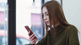 Η αρκετά νέα γυναίκα σε ένα μοντέρνο πουλόβερ κάθεται στο café, πίνει τον καφέ, τα κείμενα τα μηνύματα και τα χαμόγελα ευτυχώς απόθεμα βίντεο Η αρκετά νέα γυναίκα σε ένα μοντέρνο πουλόβερ κάθεται στο café, πίνει τον καφέ, τα κείμενα τα μηνύματα και τα χαμόγελα ευτυχώς απόθεμα βίντεο