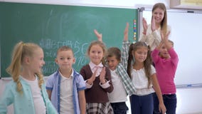 Η βασική εκπαίδευση, σχολικά παιδιά με το δάσκαλο εξετάζει τη κάμερα και επιδοκιμάζει έπειτα στο υπόβαθρο του πίνακα απόθεμα βίντεο Η βασική εκπαίδευση, σχολικά παιδιά με το δάσκαλο εξετάζει τη κάμερα και επιδοκιμάζει έπειτα στο υπόβαθρο του πίνακα απόθεμα βίντεο