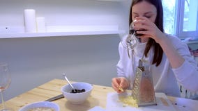 Η γυναίκα τρίβει το τυρί στον ξύστη στο σπίτι και πίνει το κόκκινο κρασί στην κουζίνα Το ζεύγος μαγειρεύει το γεύμα φιλμ μικρού μήκους Η γυναίκα τρίβει το τυρί στον ξύστη στο σπίτι και πίνει το κόκκινο κρασί στην κουζίνα Το ζεύγος μαγειρεύει το γεύμα φιλμ μικρού μήκους