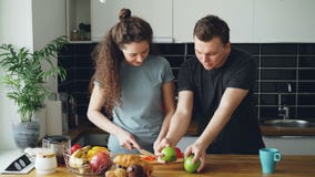 Η εύθυμη γυναίκα που προετοιμάζει το πρόγευμα στην κουζίνα, ο σύζυγός της έρχεται παίρνοντας τα μήλα και παρουσιάζοντας την που κ απόθεμα βίντεο Η εύθυμη γυναίκα που προετοιμάζει το πρόγευμα στην κουζίνα, ο σύζυγός της έρχεται παίρνοντας τα μήλα και παρουσιάζοντας την που κ απόθεμα βίντεο
