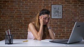 Η κουρασμένη εργαζόμενη γυναίκα χρησιμοποιεί το lap-top της, δακτυλογραφώντας καθμένος στον υπολογιστή γραφείου πέρα από το τουβλ Η κουρασμένη εργαζόμενη γυναίκα χρησιμοποιεί το lap-top της, δακτυλογραφώντας καθμένος στον υπολογιστή γραφείου πέρα από το τουβλ
