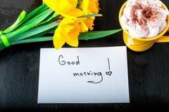 Η κούπα καφέ με το κίτρινο daffodil ανθίζει και αναφέρει τη καλημέρα στον άσπρο αγροτικό πίνακα Ημέρα μητέρων ή ημέρα των γυναικώ Στοκ φωτογραφίες με δικαίωμα ελεύθερης χρήσης Η κούπα καφέ με το κίτρινο daffodil ανθίζει και αναφέρει τη καλημέρα στον άσπρο αγροτικό πίνακα Ημέρα μητέρων ή ημέρα των γυναικώ Στοκ φωτογραφίες με δικαίωμα ελεύθερης χρήσης