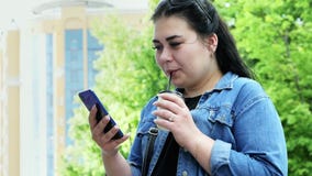 Η νέα γυναίκα σπουδαστής χρησιμοποιεί ένα κινητό τηλέφωνο και πίνει τον καφέ φιλμ μικρού μήκους Η νέα γυναίκα σπουδαστής χρησιμοποιεί ένα κινητό τηλέφωνο και πίνει τον καφέ φιλμ μικρού μήκους