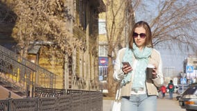 Η νέα επιχειρησιακή γυναίκα περπατά στην οδό και πίνει τον καφέ και χρησιμοποίηση του smartphone στο μεσημεριανό διάλειμμα απόθεμα βίντεο Η νέα επιχειρησιακή γυναίκα περπατά στην οδό και πίνει τον καφέ και χρησιμοποίηση του smartphone στο μεσημεριανό διάλειμμα απόθεμα βίντεο