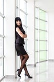 Η νέα όμορφη ευτυχής γυναίκα brunette έντυσε σε ένα μαύρο επιχειρησιακό κοστούμι με μια κοντή φούστα που στέκεται κοντά στο παράθ στοκ φωτογραφίες με δικαίωμα ελεύθερης χρήσης Η νέα όμορφη ευτυχής γυναίκα brunette έντυσε σε ένα μαύρο επιχειρησιακό κοστούμι με μια κοντή φούστα που στέκεται κοντά στο παράθ στοκ φωτογραφίες με δικαίωμα ελεύθερης χρήσης