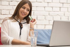 Η νέα όμορφη χαμογελώντας γυναίκα κάθεται σε έναν πίνακα και αγοράζει on-line στοκ εικόνες με δικαίωμα ελεύθερης χρήσης Η νέα όμορφη χαμογελώντας γυναίκα κάθεται σε έναν πίνακα και αγοράζει on-line στοκ εικόνες με δικαίωμα ελεύθερης χρήσης