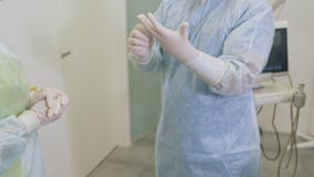 Η νοσοκόμα βοηθά έναν χειρούργο για να βάλει στα αποστειρωμένα γάντια πριν από τη sclerotherapy χειρουργική επέμβαση στο νοσοκομε φιλμ μικρού μήκους Η νοσοκόμα βοηθά έναν χειρούργο για να βάλει στα αποστειρωμένα γάντια πριν από τη sclerotherapy χειρουργική επέμβαση στο νοσοκομε φιλμ μικρού μήκους
