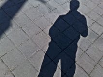 Η σκιά ενός ατόμου σε ένα κεραμίδι πεζοδρομίων σε ένα πάρκο στοκ εικόνα Η σκιά ενός ατόμου σε ένα κεραμίδι πεζοδρομίων σε ένα πάρκο στοκ εικόνα