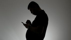 Η σκιαγραφία ενός ατόμου με μια κυρτή σπονδυλική στήλη Ένα κεκλιμένο άτομο με ένα κινητό τηλέφωνο στα χέρια του απόθεμα βίντεο Η σκιαγραφία ενός ατόμου με μια κυρτή σπονδυλική στήλη Ένα κεκλιμένο άτομο με ένα κινητό τηλέφωνο στα χέρια του απόθεμα βίντεο