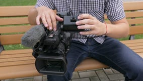 Η συνεδρίαση καμεραμάν στον πάγκο κοιτάζει βιαστικά το μήκος σε πόδηα στη τηλεοπτική κάμερα φιλμ μικρού μήκους Η συνεδρίαση καμεραμάν στον πάγκο κοιτάζει βιαστικά το μήκος σε πόδηα στη τηλεοπτική κάμερα φιλμ μικρού μήκους