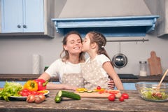 Η χαριτωμένη κόρη φιλά mom στο μάγουλό της μαγειρεύοντας σε μια όμορφη μ στοκ φωτογραφίες Η χαριτωμένη κόρη φιλά mom στο μάγουλό της μαγειρεύοντας σε μια όμορφη μ στοκ φωτογραφίες