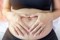 Η όμορφη έγκυος γυναίκα κάνει το σύμβολο της αγάπης και σχετικά με στην κοιλιά της Το έγκυο κορίτσι έχει το πρώτο παιδί της οικογ στοκ εικόνες Η όμορφη έγκυος γυναίκα κάνει το σύμβολο της αγάπης και σχετικά με στην κοιλιά της Το έγκυο κορίτσι έχει το πρώτο παιδί της οικογ στοκ εικόνες