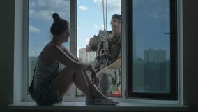 Η όμορφη γυναίκα κάθεται στο windowsill και τις συζητήσεις με το steeplejack έξω από το παράθυρο απόθεμα βίντεο Η όμορφη γυναίκα κάθεται στο windowsill και τις συζητήσεις με το steeplejack έξω από το παράθυρο απόθεμα βίντεο