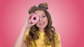 Η όμορφη τοποθέτηση νέων κοριτσιών με doughnut κλείνουν το μάτι και η εξέταση χαμόγελου τη κάμερα σε ένα ρόδινο υπόβαθρο φιλμ μικρού μήκους Η όμορφη τοποθέτηση νέων κοριτσιών με doughnut κλείνουν το μάτι και η εξέταση χαμόγελου τη κάμερα σε ένα ρόδινο υπόβαθρο φιλμ μικρού μήκους