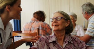 Θηλυκός γιατρός που γονατίζει μιλώντας στη με ειδικές ανάγκες ανώτερη γυναίκα στην αναπηρική καρέκλα 4k απόθεμα βίντεο Θηλυκός γιατρός που γονατίζει μιλώντας στη με ειδικές ανάγκες ανώτερη γυναίκα στην αναπηρική καρέκλα 4k απόθεμα βίντεο