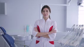 Θηλυκός οδοντίατρος που στέκεται και που χαμογελά στη κάμερα τα όπλα που διασχίζονται με απόθεμα βίντεο Θηλυκός οδοντίατρος που στέκεται και που χαμογελά στη κάμερα τα όπλα που διασχίζονται με απόθεμα βίντεο