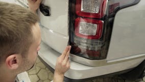 Κλείστε επάνω γυρισμένος των χεριών ατόμων ` s unstick την ταινία με το άσπρο ακριβό αυτοκίνητο καλυπτρών απόθεμα βίντεο Κλείστε επάνω γυρισμένος των χεριών ατόμων ` s unstick την ταινία με το άσπρο ακριβό αυτοκίνητο καλυπτρών απόθεμα βίντεο