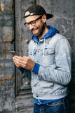 Κάθετο πορτρέτο του τύπου hipster στο πουκάμισο τζιν, την ΚΑΠ και το eyewear σύγχρονο τηλέφωνο εκμετάλλευσης στα χέρια του που έχ στοκ εικόνα με δικαίωμα ελεύθερης χρήσης Κάθετο πορτρέτο του τύπου hipster στο πουκάμισο τζιν, την ΚΑΠ και το eyewear σύγχρονο τηλέφωνο εκμετάλλευσης στα χέρια του που έχ στοκ εικόνα με δικαίωμα ελεύθερης χρήσης