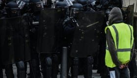 Κίτρινες φανέλλες - Gilets jaunes διαμαρτύρεται - διαμαρτυρόμενος που στέκεται μόνο μπροστά από την αστυνομία ταραχής στοκ εικόνα Κίτρινες φανέλλες - Gilets jaunes διαμαρτύρεται - διαμαρτυρόμενος που στέκεται μόνο μπροστά από την αστυνομία ταραχής στοκ εικόνα