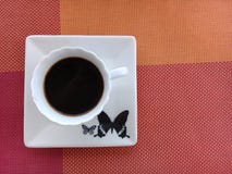 Καφές πάνω από ένα πιατάκι με το σχέδιο πεταλούδων στοκ εικόνα Καφές πάνω από ένα πιατάκι με το σχέδιο πεταλούδων στοκ εικόνα