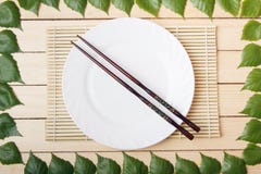Κενό πιάτο σε ένα χαλί μπαμπού με chopsticks, τοπ άποψη, σε ένα ξύλινο υπόβαθρο, που πλαισιώνεται με τα φύλλα ενός δέντρου στοκ φωτογραφίες Κενό πιάτο σε ένα χαλί μπαμπού με chopsticks, τοπ άποψη, σε ένα ξύλινο υπόβαθρο, που πλαισιώνεται με τα φύλλα ενός δέντρου στοκ φωτογραφίες