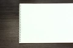 Κενό σημειωματάριο για τη σκιαγράφηση με τις άσπρες σελίδες στο μαύρο ξύλινο πίνακα στοκ φωτογραφία με δικαίωμα ελεύθερης χρήσης Κενό σημειωματάριο για τη σκιαγράφηση με τις άσπρες σελίδες στο μαύρο ξύλινο πίνακα στοκ φωτογραφία με δικαίωμα ελεύθερης χρήσης