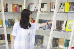 Κινεζικό πορτρέτο της νέας όμορφης επίτευξης γυναικών για ένα βιβλίο βιβλιοθηκών στο βιβλιοπωλείο Στοκ Φωτογραφία Κινεζικό πορτρέτο της νέας όμορφης επίτευξης γυναικών για ένα βιβλίο βιβλιοθηκών στο βιβλιοπωλείο Στοκ Φωτογραφία