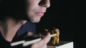 Κινηματογράφηση σε πρώτο πλάνο ενός ατόμου που τρώει τα νουντλς με chopsticks από ένα κιβώτιο Ευρωπαϊκά τρόφιμα κατανάλωσης απόθεμα βίντεο Κινηματογράφηση σε πρώτο πλάνο ενός ατόμου που τρώει τα νουντλς με chopsticks από ένα κιβώτιο Ευρωπαϊκά τρόφιμα κατανάλωσης απόθεμα βίντεο